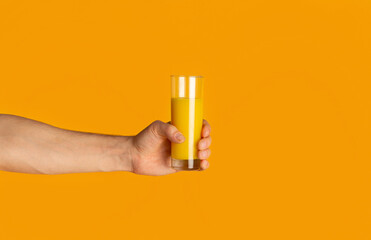 Wall Mural - Closeup of young guy holding glass with fresh orange juice on color background, empty space