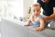 © Nastya - Cute little baby boy with big blue eyes try stand up on sofa, father help him