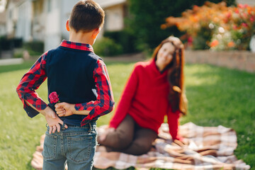 Wall Mural - Elegant woman in a autumn park. Family near house. Mother sitting on a plaid. The boy gives flowers to his mother