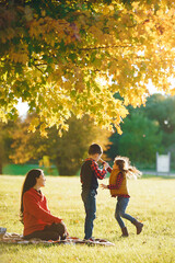 Wall Mural - Cute family in a autumn park. Happy mother with little kids. Family playing on yellow leaves. Golden autumn.