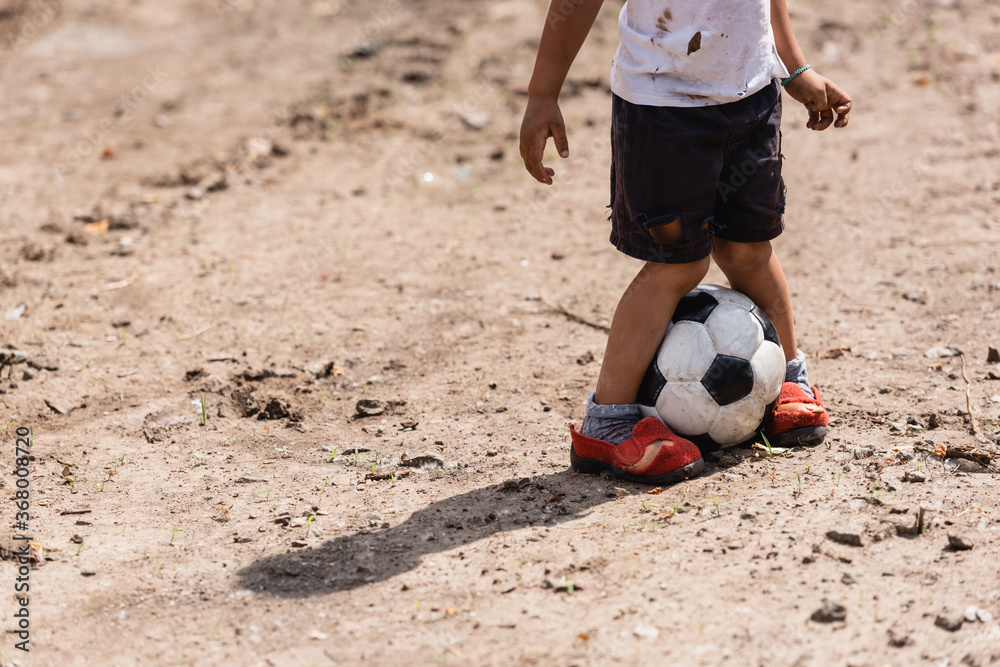 Cropped view of destitute african american child playing football on ...