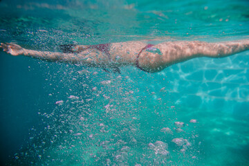  young woman diving floating in a pool. summer and fun lifestyle. selective focus on bubbles.