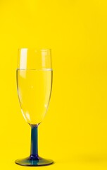 Poster - Vertical sot of a wine glass with clear water against a yellow background