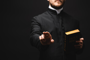 Canvas Print - selective focus of priest holding holy bible while gesturing isolated on black