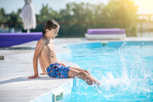 Smiling Boy Sitting On Poolside His Feet In Water