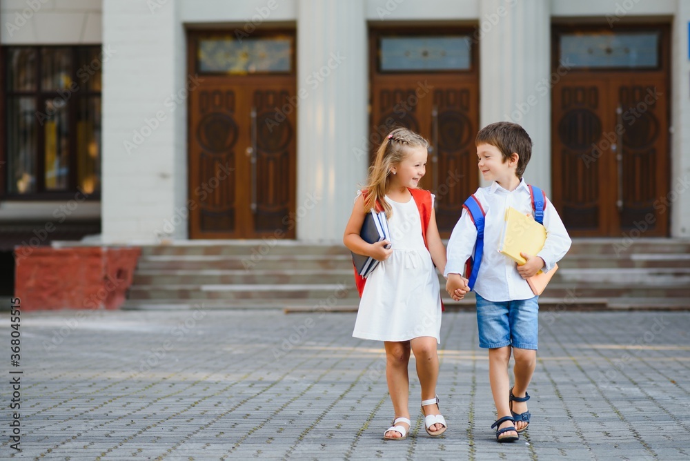 Happy children - boy and girl with books and backpacks on the first school day. Excited to be back to school after vacation. Full length outdoor portrait.