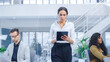 © Gorodenkoff - In the Bright Corporate Office: Female Executive Holding Digital Tablet Computer Walks Through the Office Where Her Professional Staff of Businesspeople Work on Desktop Computers