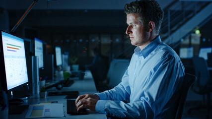 Poster - Portrait of Ambitious and Confident Businessman Uses Desktop Computer, Typing on a Keyboard, Monitoring Business Transactions, Signing Contracts. Works Late at Night in Big Corporate Office