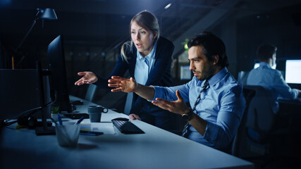 Aufkleber - Confident Businessman Uses Desktop Computer, His Female Manager Explains Specific Tasks, Account Handling and Strategy. Professional People Debating and Arguing Late at Night in Corporate Office.