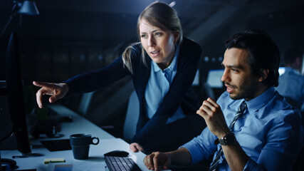 Poster - Confident Businessman Uses Desktop Computer, His Female Manager Explains Specific Tasks, Account Handling and Strategy. Professional People Debating and Arguing Late at Night in Corporate Office.