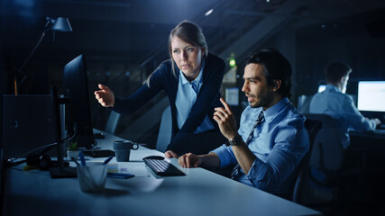 Aufkleber - Confident Businessman Uses Desktop Computer, His Female Manager Explains Specific Tasks, Account Handling and Strategy. Professional People Debating and Arguing Late at Night in Corporate Office.