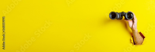 Cuadros en Lienzo Female hand holds black binoculars on yellow background, travel, find and search concept