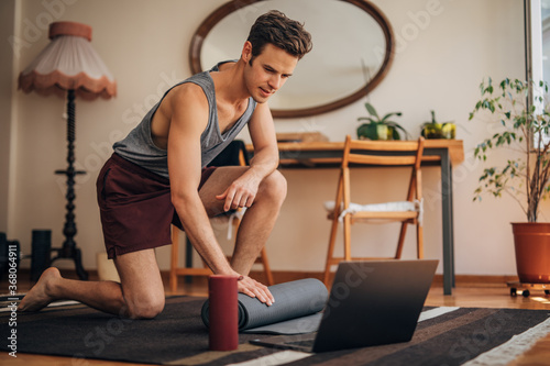 Young man preparing exercise mat for his online yoga class