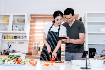 Asian couples Do activities together by cooking which learning from the instruction in the application On mobile phones, concept to people and education online.