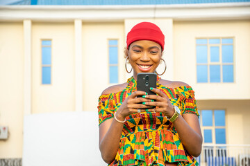 Poster - pretty young african woman smiling and using her mobile phone outdoor