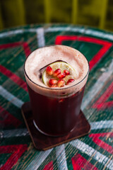 Wall Mural - A cocktail in a highball glass with foam, ice cube inside, garnished with a lime wheel and pomegranate seeds