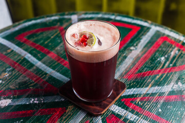 Wall Mural - A cocktail in a highball glass with foam, ice cube inside, garnished with a lime wheel and pomegranate seeds