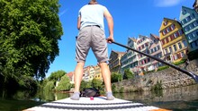 Rear-view Of A Man Riding His Stand Up Paddle Board (SUP) Down The Neckar River Along The Picturesque Old Town Of Tübingen In Southern Germany