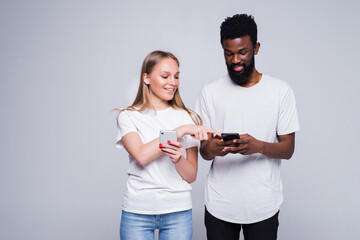 Smiling african American man talk show news on smartphone to beautiful Caucasian woman, happy multiracial diverse young people isolated on gray studio background using cellphones together