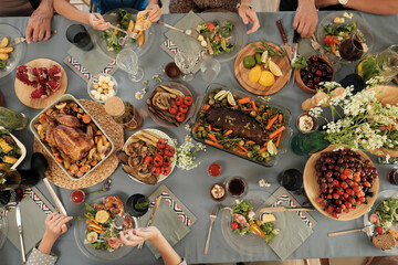 Wall Mural - High angle view of festive table with different delicious dishes with people sitting around and eating