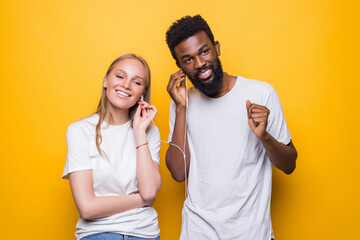 Portrait of joyful couple african man and caucsian woman singing while using smartphone and earphones together over yellow background