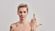 No way. Portrait of arrogant half naked tattooed woman with pierced nose and short hair showing middle finger sign, looking at camera isolated over light background