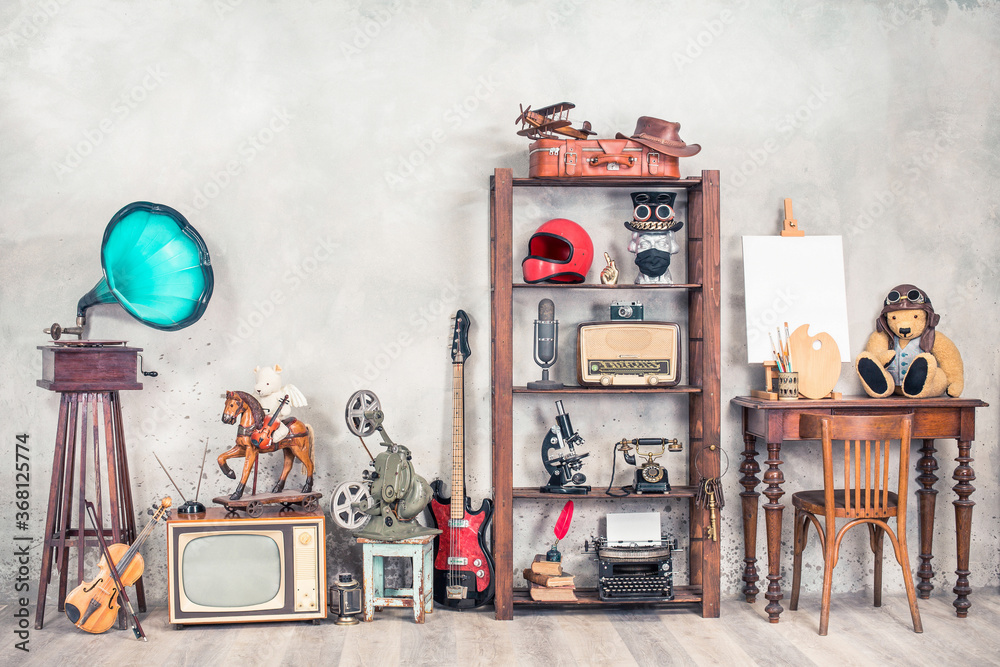 Antique media devices, writers tools, gramophone, film projector, old Teddy Bear toys and white canvas blank on easel, violin and guitar front concrete wall background. Vintage style filtered photo - obrazy, fototapety, plakaty 