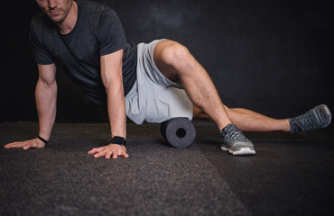 Athletic man using a foam roller to relieve sore muscles and recovers by massaging fascia after a workout.