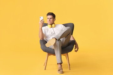 Young man taking selfie while relaxing in armchair against color background