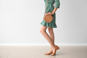 Beautiful young woman with wicker bag near light wall