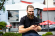 © F8  \ Suport Ukraine - Casual hipster man with a beard and casual clothes sitting on an urban bench texting on his mobile phone