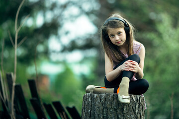 Wall Mural - Little cute girl in headphones sitting on a stump in the village.