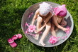 Happy children take a bath in the garden, with peony flowers. Two little sisters bathe with pink flowers in a round basin, outdoors