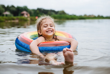 happy child swims in the river on a colored inflatable circle. cute little girl gives birth while sw