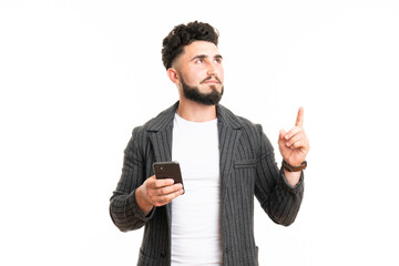 Portrait of an excited young man in casual using mobile phone while pointing finger up isolated over white background