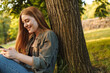 © Drobot Dean - Young blonde woman using smartphone under tree in park