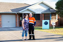 Happy Middle Aged Couple Standing Infront Of House With Sold Real Estate Sign