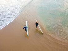 Looking Down On Two Surfers Walking On A Beach Between Waves