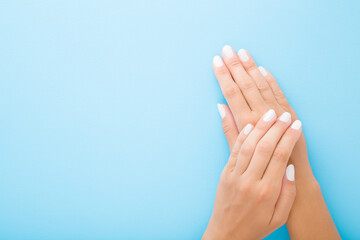 Wall Mural - Young woman hands with white nails on light blue table background. Pastel color. Point of view shot. Closeup. Soft touch. Empty place for text. Top down view.