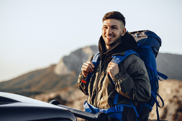 Portrait of a young traveler man in hiking equipment standing near his off-road car