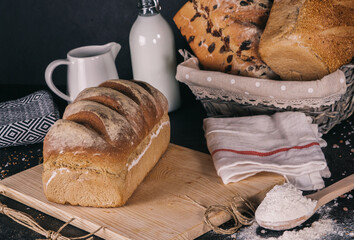 Assortment of baked bread and bread rolls on black table black background.