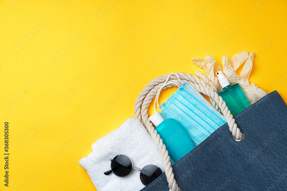 Blue beach bag with beach accessories and protective mask on yellow background - obrazy, fototapety, plakaty 