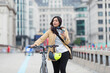 © Paul Bradbury/Caia Image - Woman with smart phone walking bicycle on urban bridge