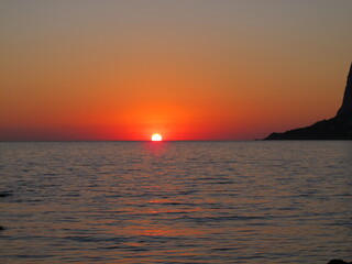 A picturesque sunset, the sun sets on the horizon in the sea. Red sunset sky, silhouettes of seagulls against the setting sun on the horizon, summer evening on the seaside