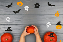 Orange Pumpkins On A Gray Background. Baby Hands On A Gray Background With Orange Pumpkins. Bats, White And Black Ghosts, Witch Hat. View From Above. Halloween Concept.