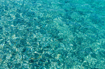 Natural background of transparent azure sea water and bottom with rocks. A close-up view of the pebbles on the beach. Blue bottom of the Mediterranean sea with small stones through clear water