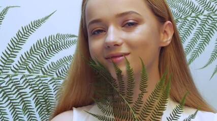 Wall Mural - Beautiful girl in tropical leaves in the studio touches her face, the concept of natural cosmetics. Blonde looking at camera smiling