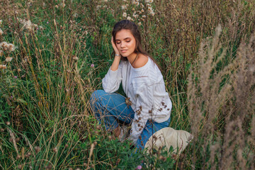 Young beautiful brunette woman sitting on the grass, smiling and touching her hair