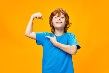 strong red-haired boy in a blue t-shirt on a yellow background 