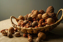 Nuts In A Basket. Beautiful Still Life Close-up On A Dark Background. Walnut, Hazelnuts (hazel), Pine Nuts, Pecans, Pine Cones.